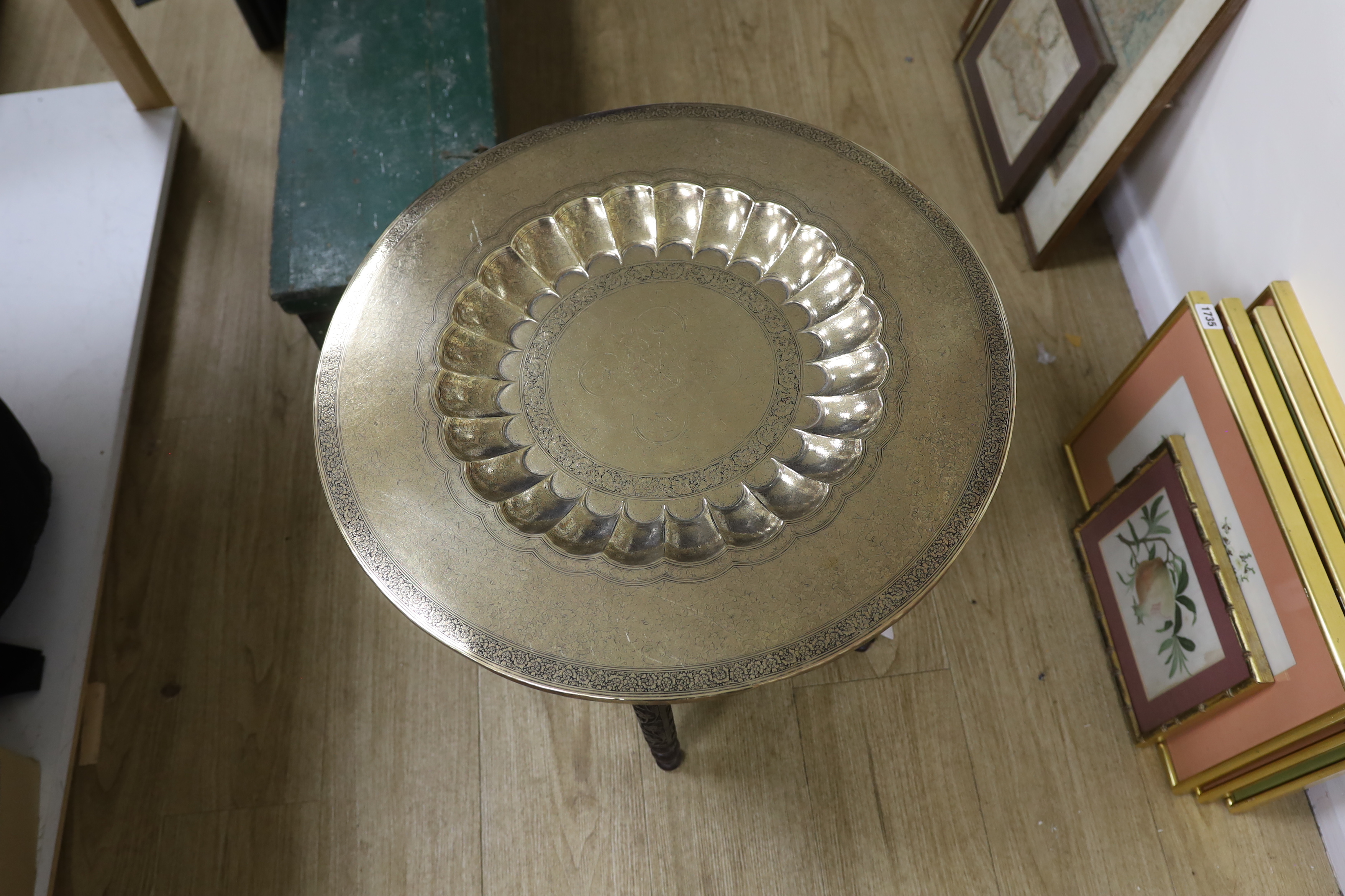 A Persian brass engraved tray top table on folding carved wood base, 59cm in diameter